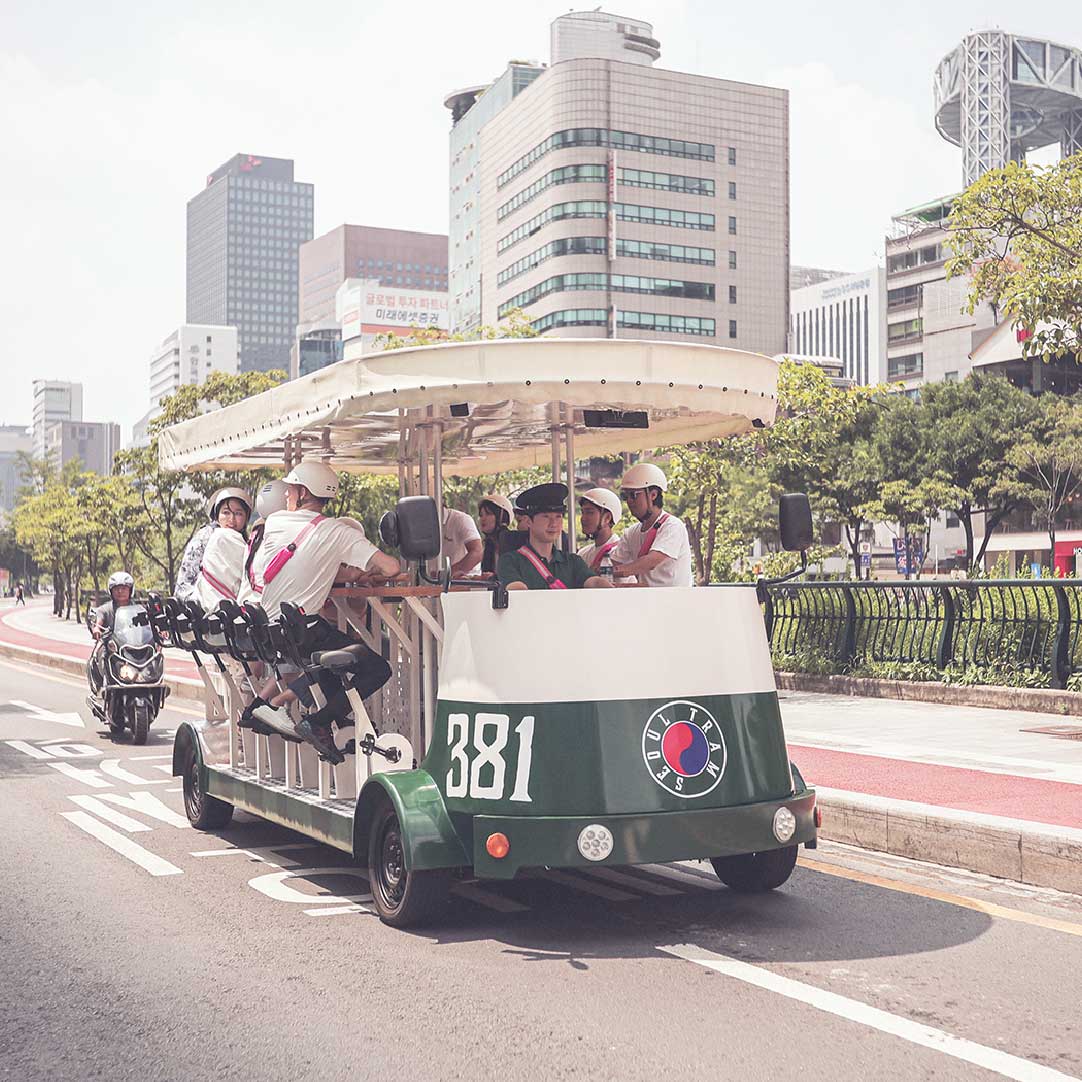 “Seoul Tram No. 381 carrying tourists through the historic downtown with skyscrapers in the background.” “首尔381号电车载着游客穿梭在市中心历史街区，高楼林立背景下尽显复古魅力。”