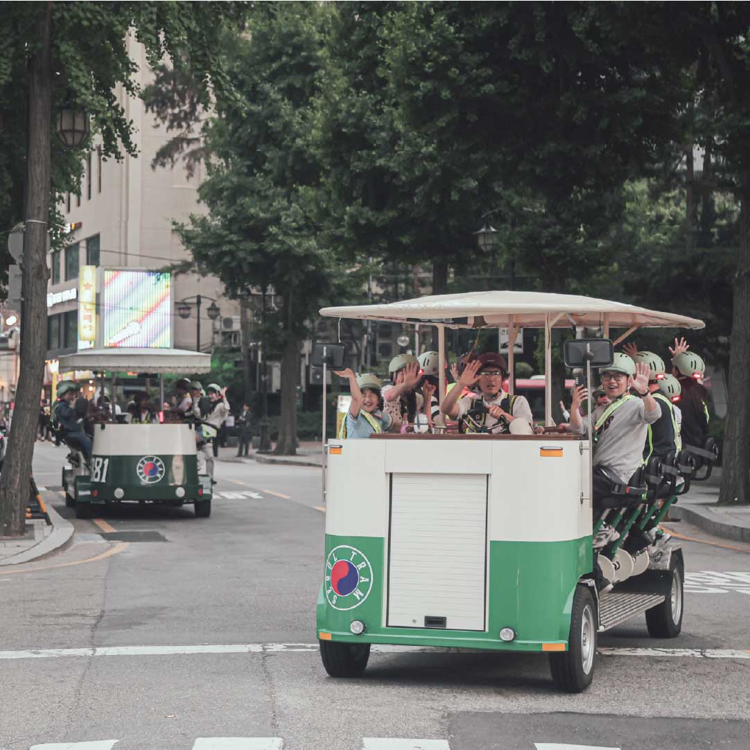 Two Seoul Trams filled with guests waving while riding through downtown Seoul in summer 两辆满载游客的首尔电车在市中心街头行驶，游客热情挥手